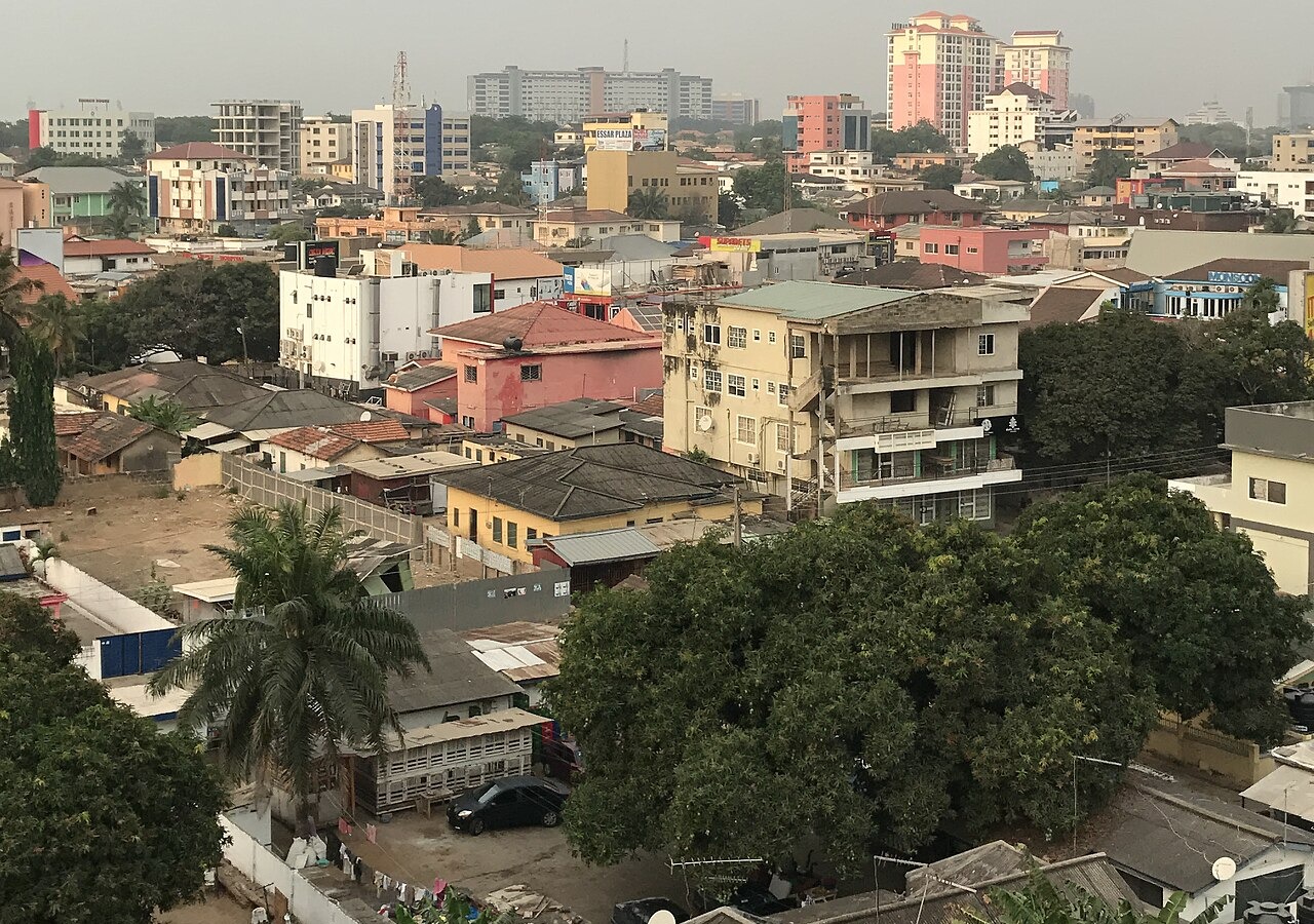 Rooftops and apartment blocks with trees and mid-rise towers in the distance in a Ghanaian city