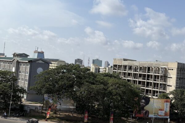 Government and office buildings with trees and an unfinished block under construction in central Accra, Ghana, under a partly cloudy sky