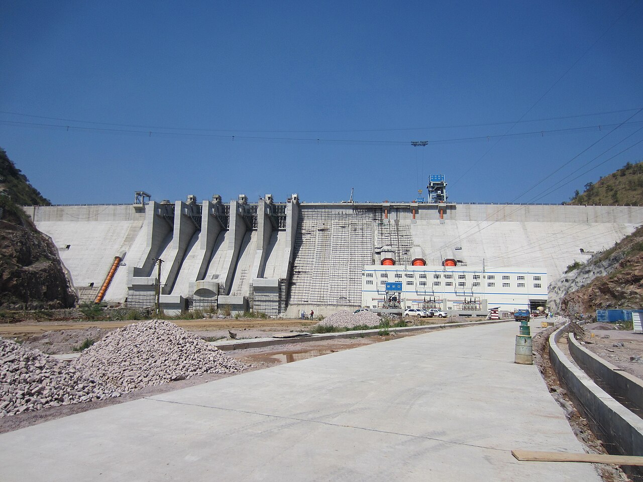 Concrete wall of the Bui hydropower dam in Ghana with spillways and a white powerhouse under a blue sky