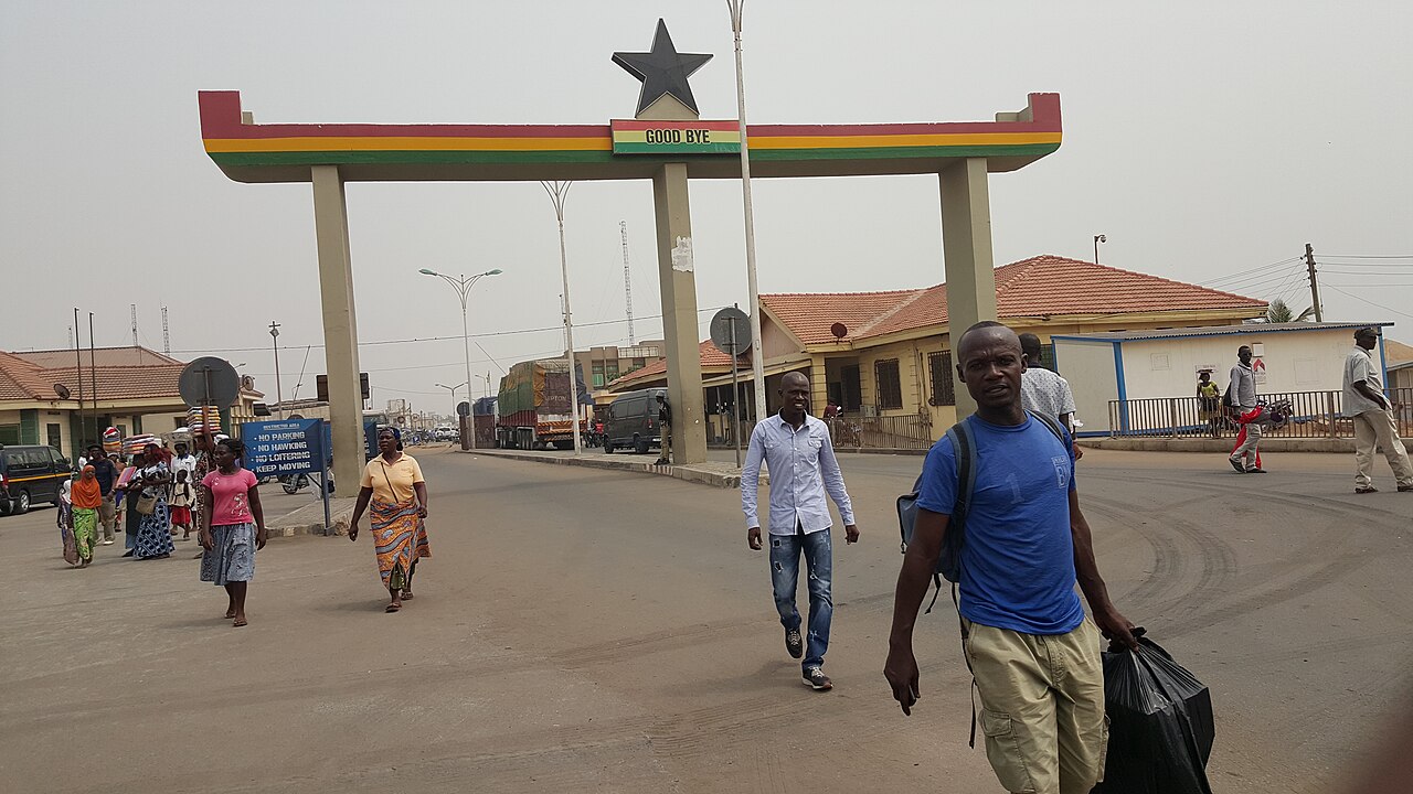 Pedestrians walk beneath a red, gold and green arch with a black star and a Good Bye sign at the Aflao border post between Ghana and Togo