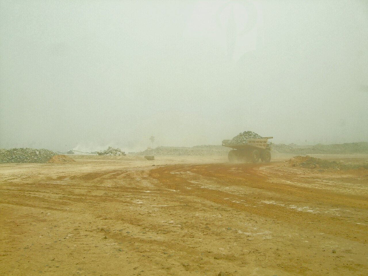 A yellow dump truck carrying rock on a dusty haul road at the Ahafo gold mine in Ghana