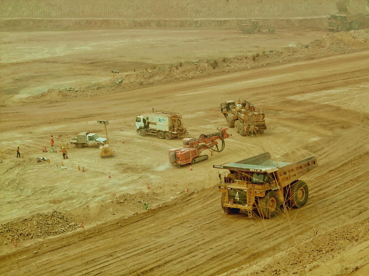 A yellow haul truck, a drill rig, a water tanker and workers in orange vests on the floor of the Ahafo open-pit gold mine in Ghana