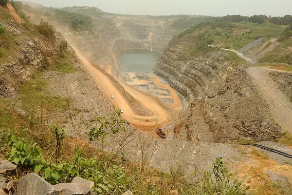Open-pit gold mine at Damang in Ghana with terraced walls, a haul road and a pool of water at the bottom