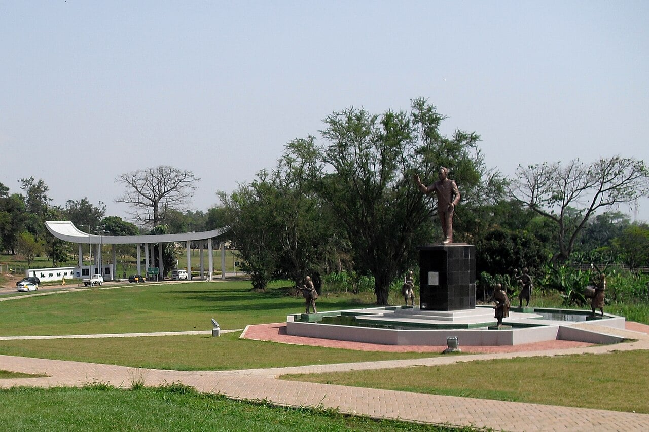 Kwame Nkrumah statue and fountain in a park beside the arched main gate of a university campus in Kumasi, Ghana