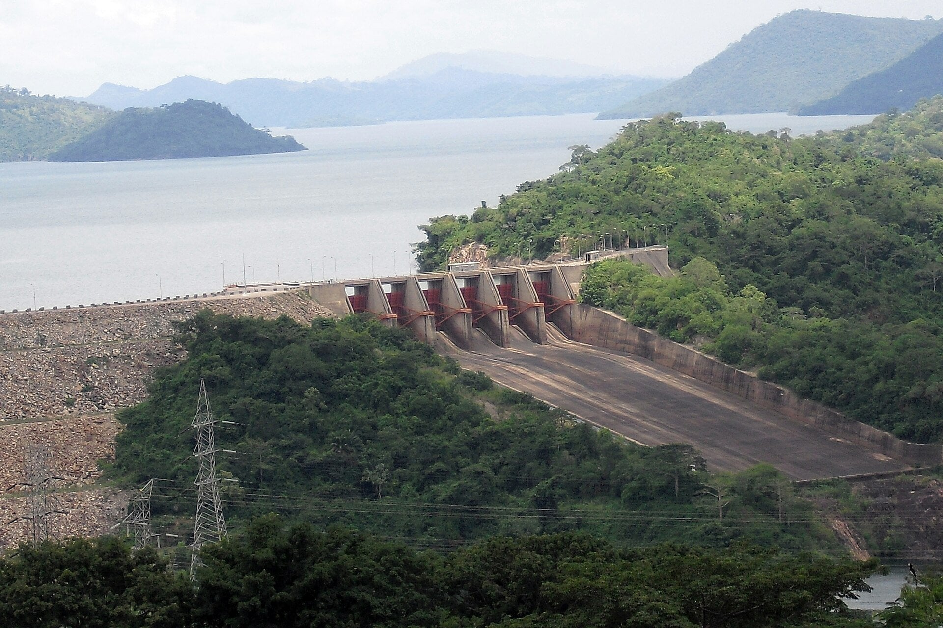 Concrete spillway with six floodgates of the Akosombo Dam on the Volta River in Ghana, with Lake Volta and green hills behind