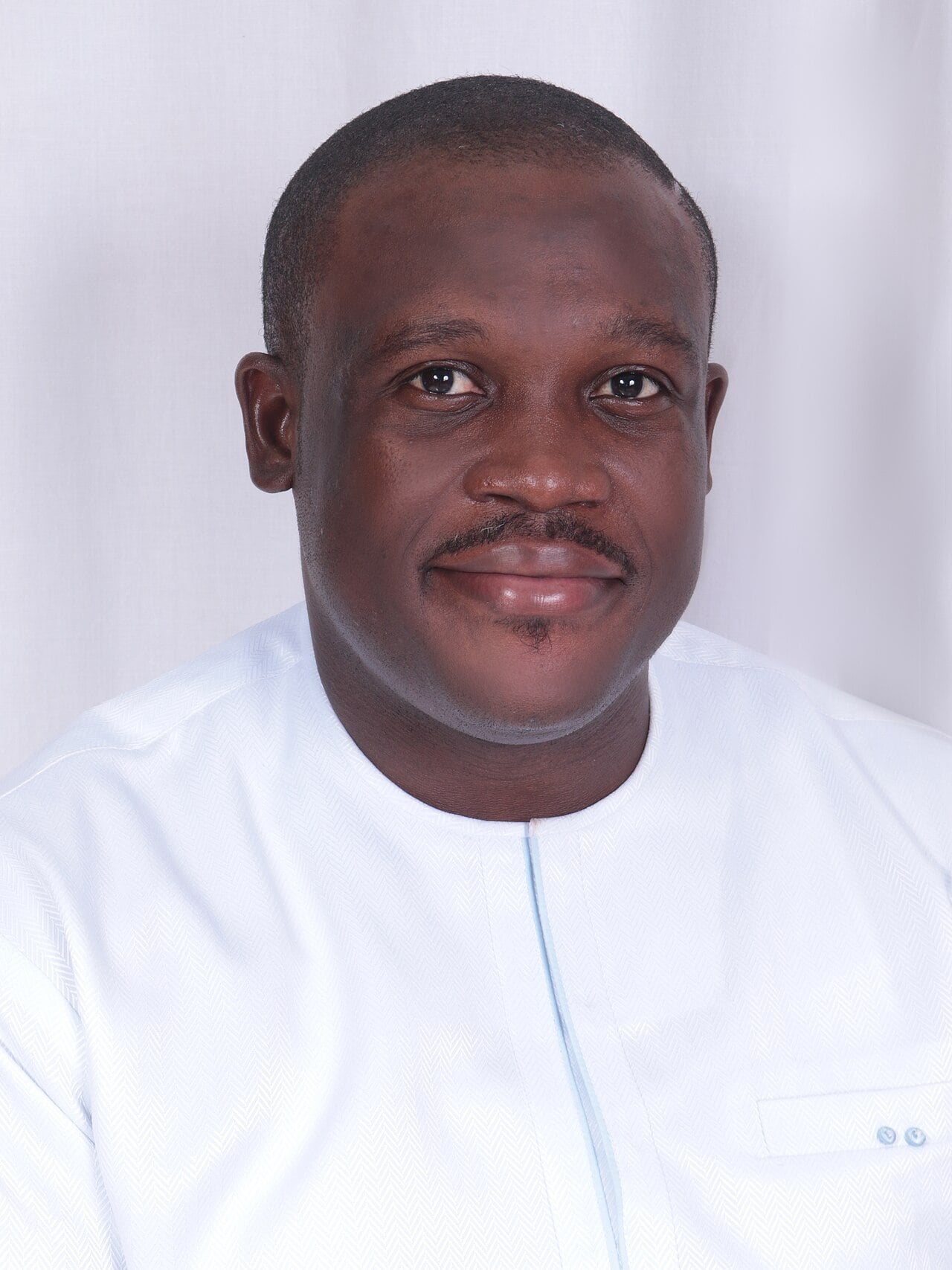 Portrait of Samuel Nartey George in a white collarless shirt against a pale background
