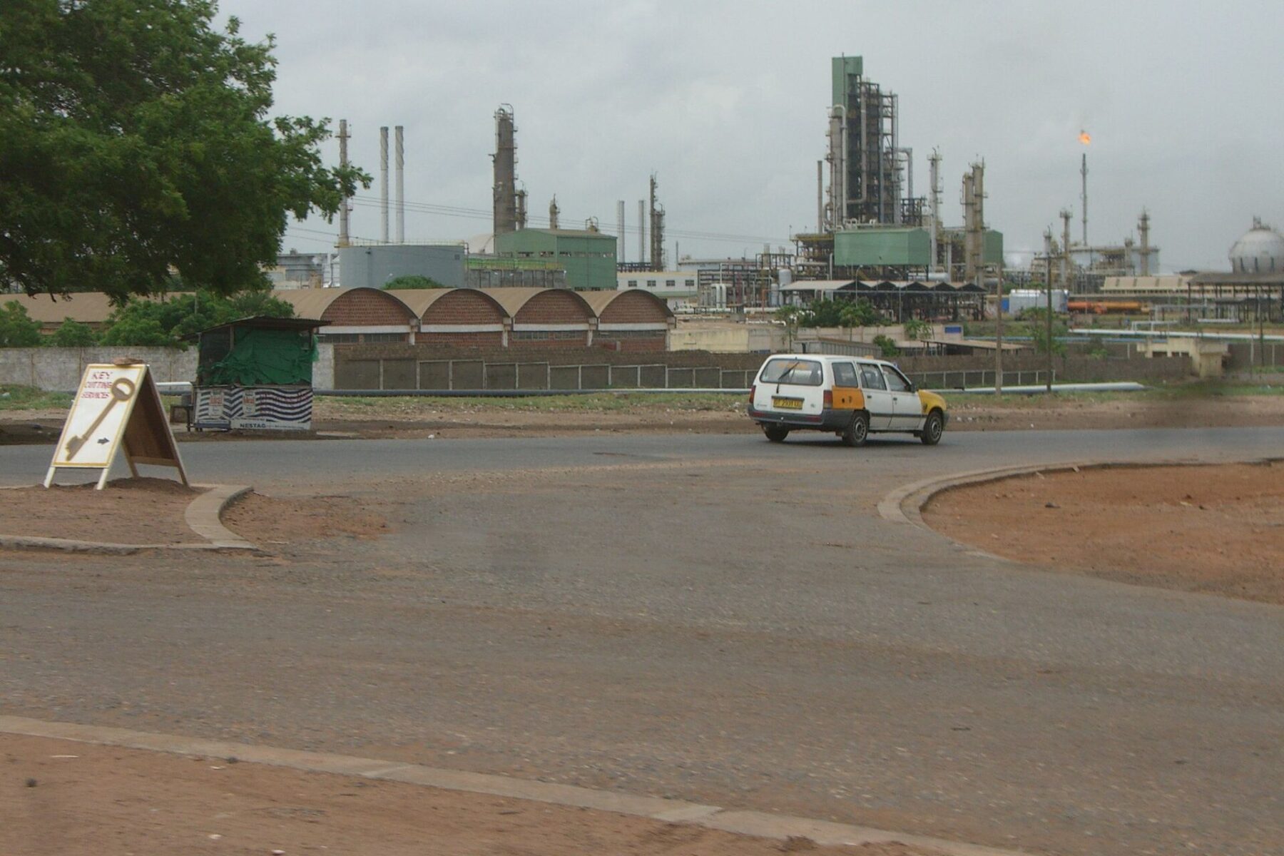 Oil refinery towers and a gas flare at Tema, Ghana, with a taxi on the road in front