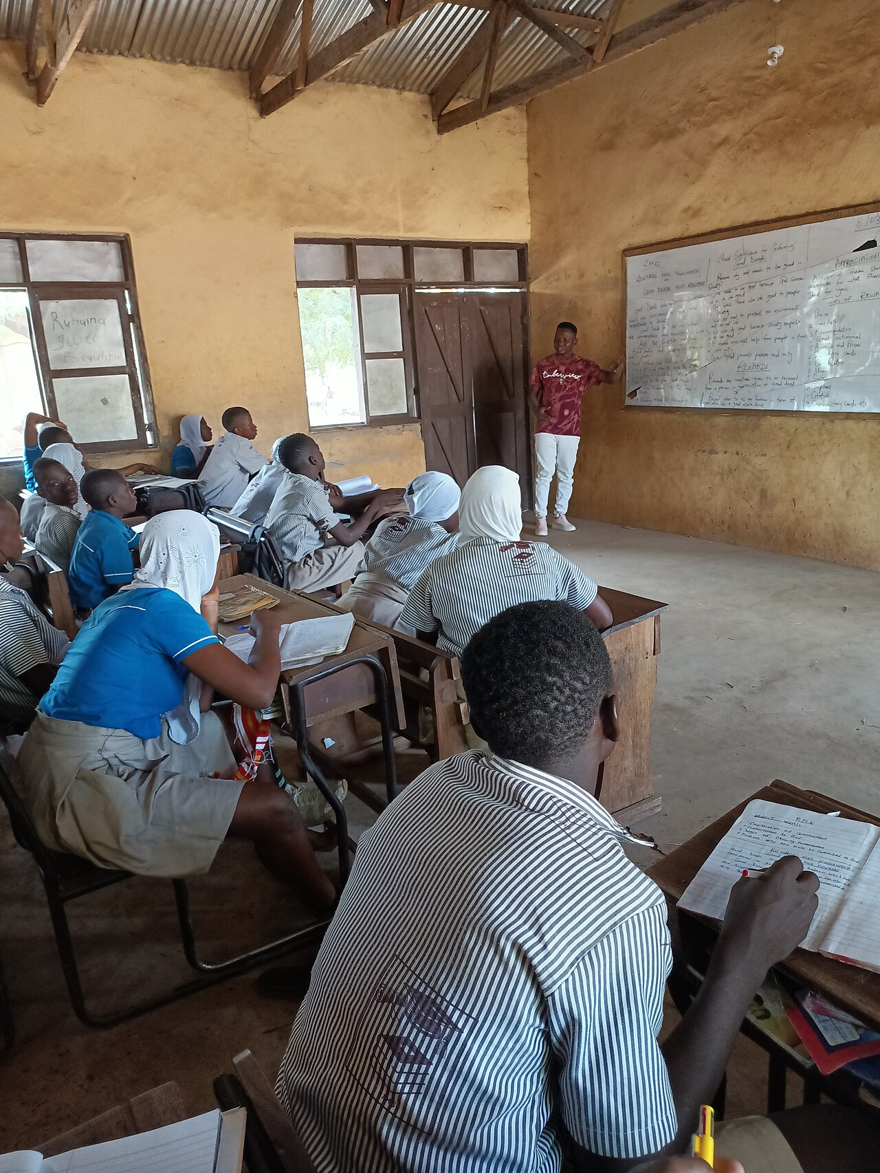 A teacher at a whiteboard teaching a class of uniformed students in a classroom in northern Ghana