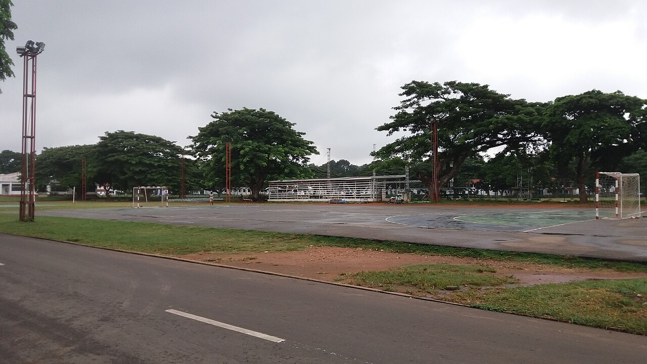 An empty sports court with football goals and a covered stand among large trees at the University of Ghana in Legon, on a cloudy day