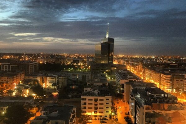 Rabat city lights at dusk under a stormy evening sky, with a glass office tower rising above apartment blocks
