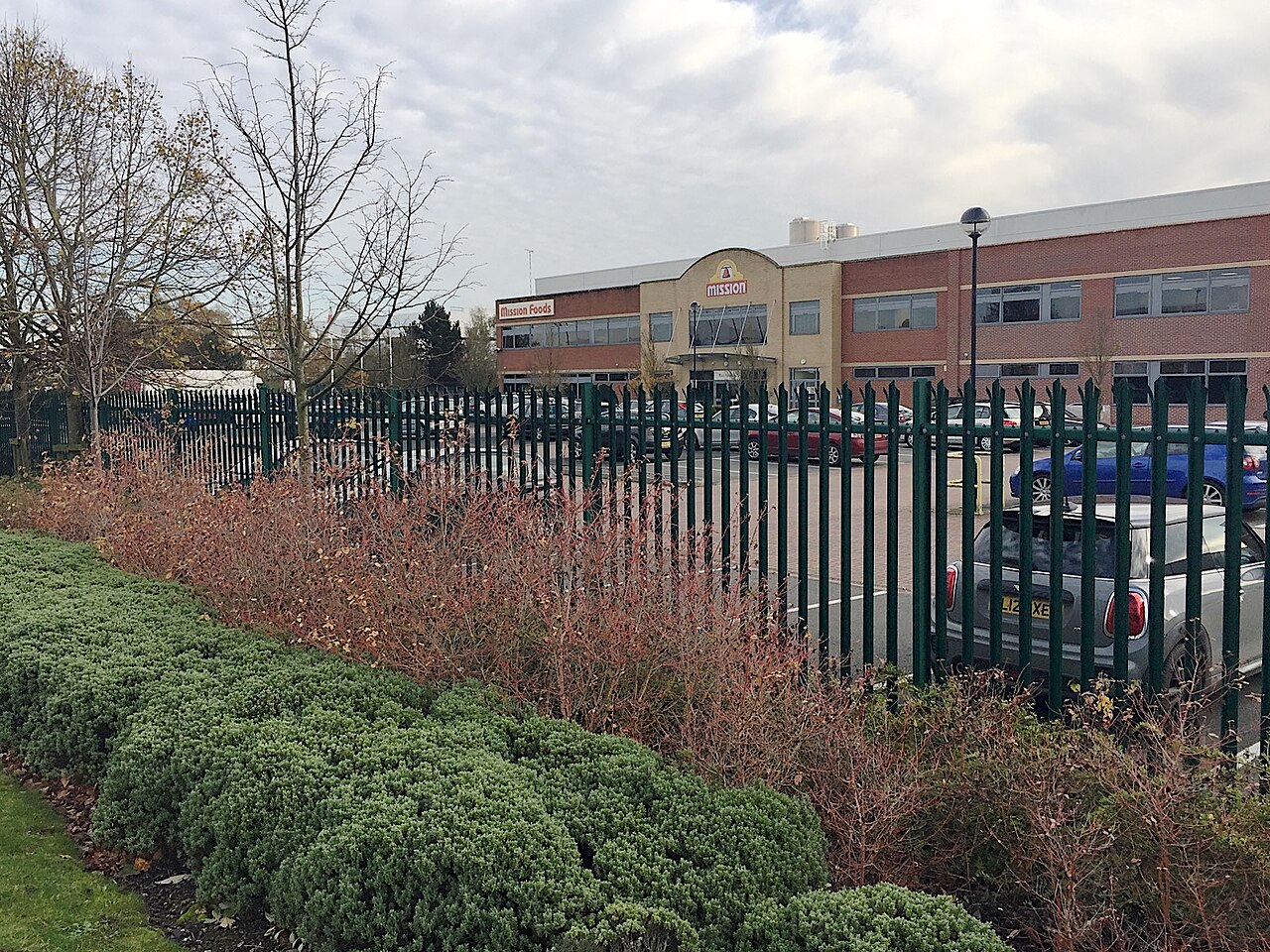 Brick office and plant building with a Mission Foods sign behind a green metal fence and hedges