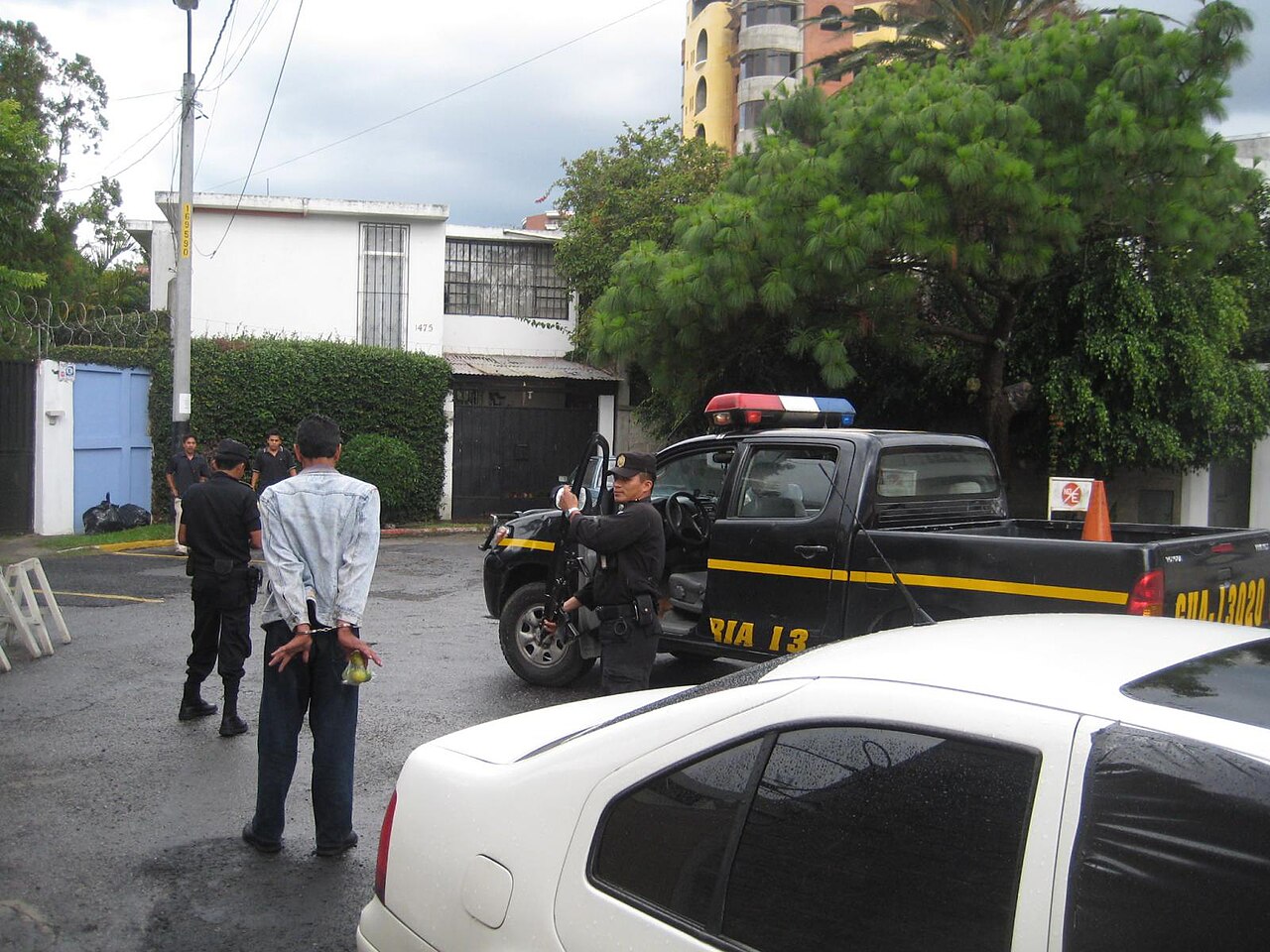 Guatemalan National Civil Police officers in black uniforms stand beside a black police pickup truck on a residential street