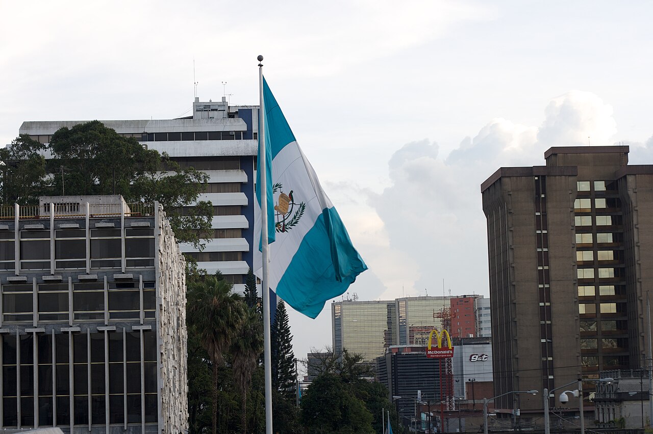 Guatemala's national flag flying in front of the tourism agency tower and office buildings in central Guatemala City