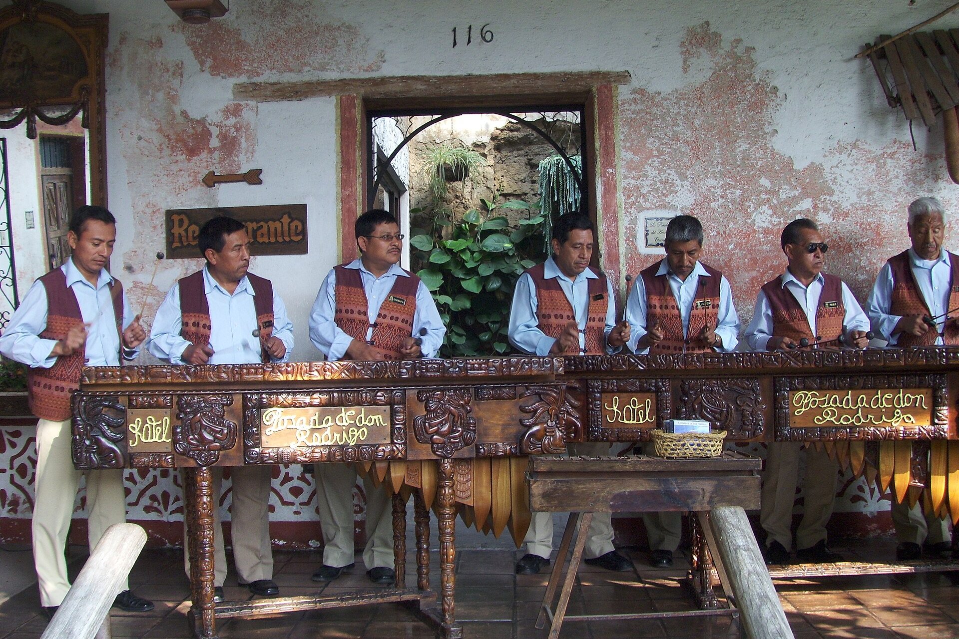 Musicians in matching vests play large carved wooden marimbas on a hotel veranda in Antigua Guatemala