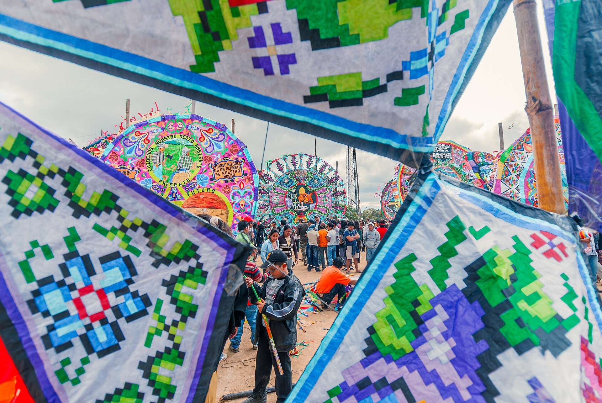 Visitors stand among giant round kites with bright patterns and an environmental message at Guatemala's 1 November kite festival