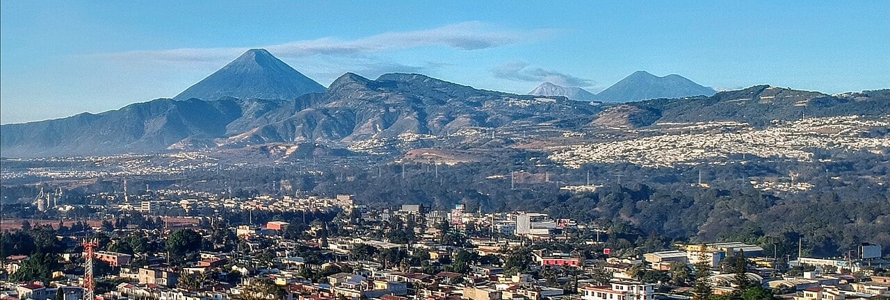 Rooftops of Villa Nueva in the foreground with a range of hills and volcanic peaks rising behind under a clear blue sky