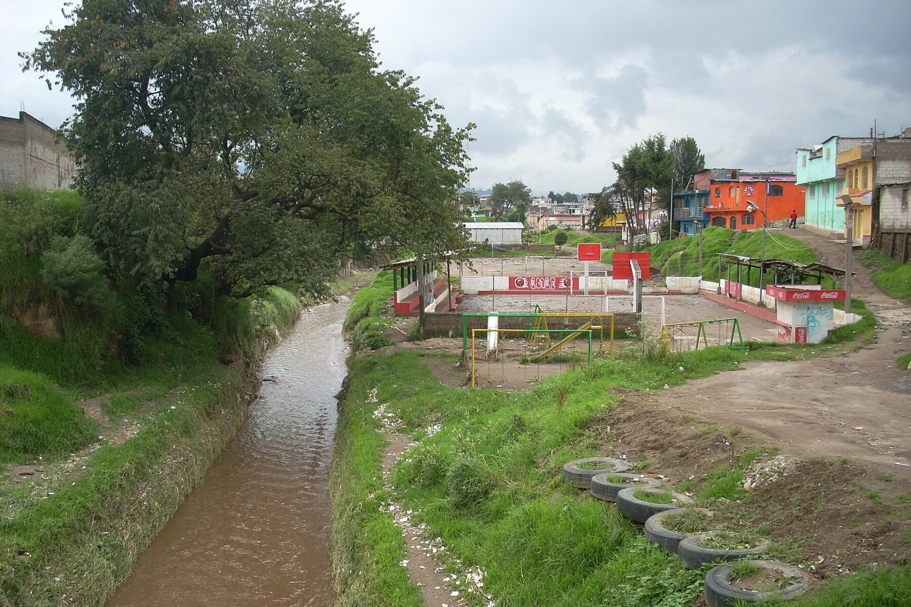 Muddy runoff in the Río Seco channel in Quetzaltenango, Guatemala, after a tropical depression, beside a mud-covered sports court