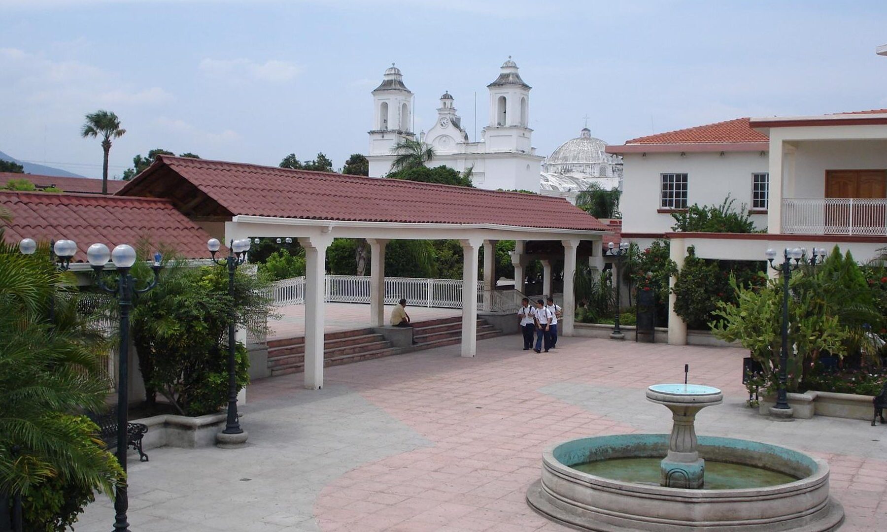 Central plaza of Zacapa, Guatemala, with a fountain, covered walkway and the white church towers behind