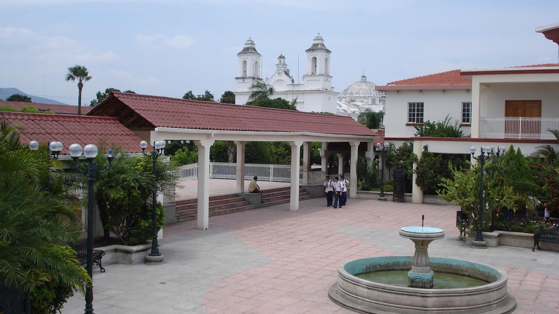 Central plaza of Zacapa, Guatemala, with a fountain, covered walkway and the white church towers behind