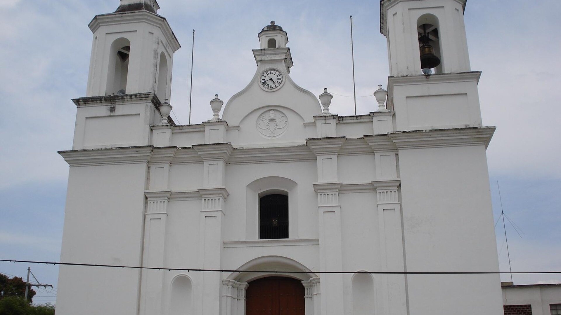 White colonial-style church front with two bell towers and a clock in the town of Zacapa, Guatemala