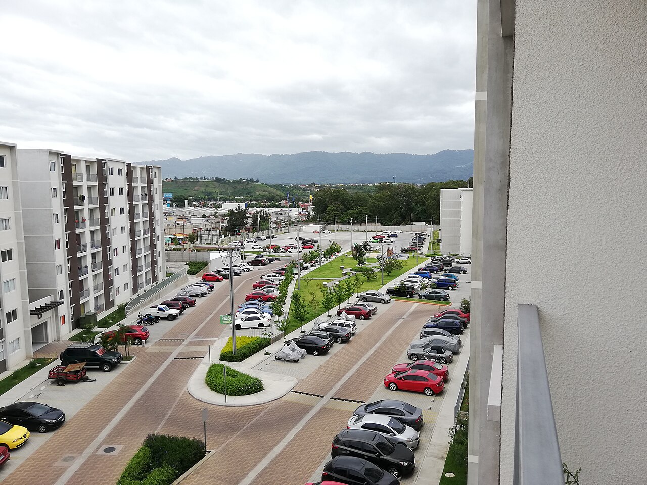 Apartment blocks and a car park in a residential complex in Villa Nueva with green hills in the distance under an overcast sky