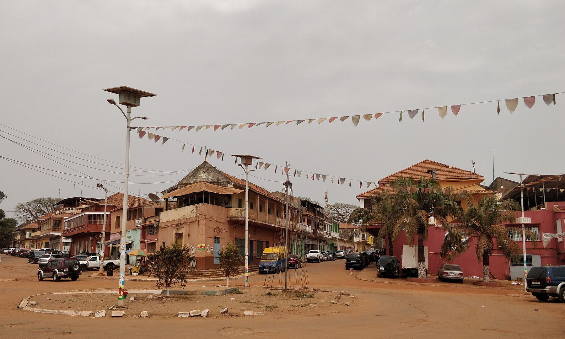 A street corner in Bissau Velho, the old centre of Bissau, with colonial-era buildings, parked cars and strings of coloured bunting across the road