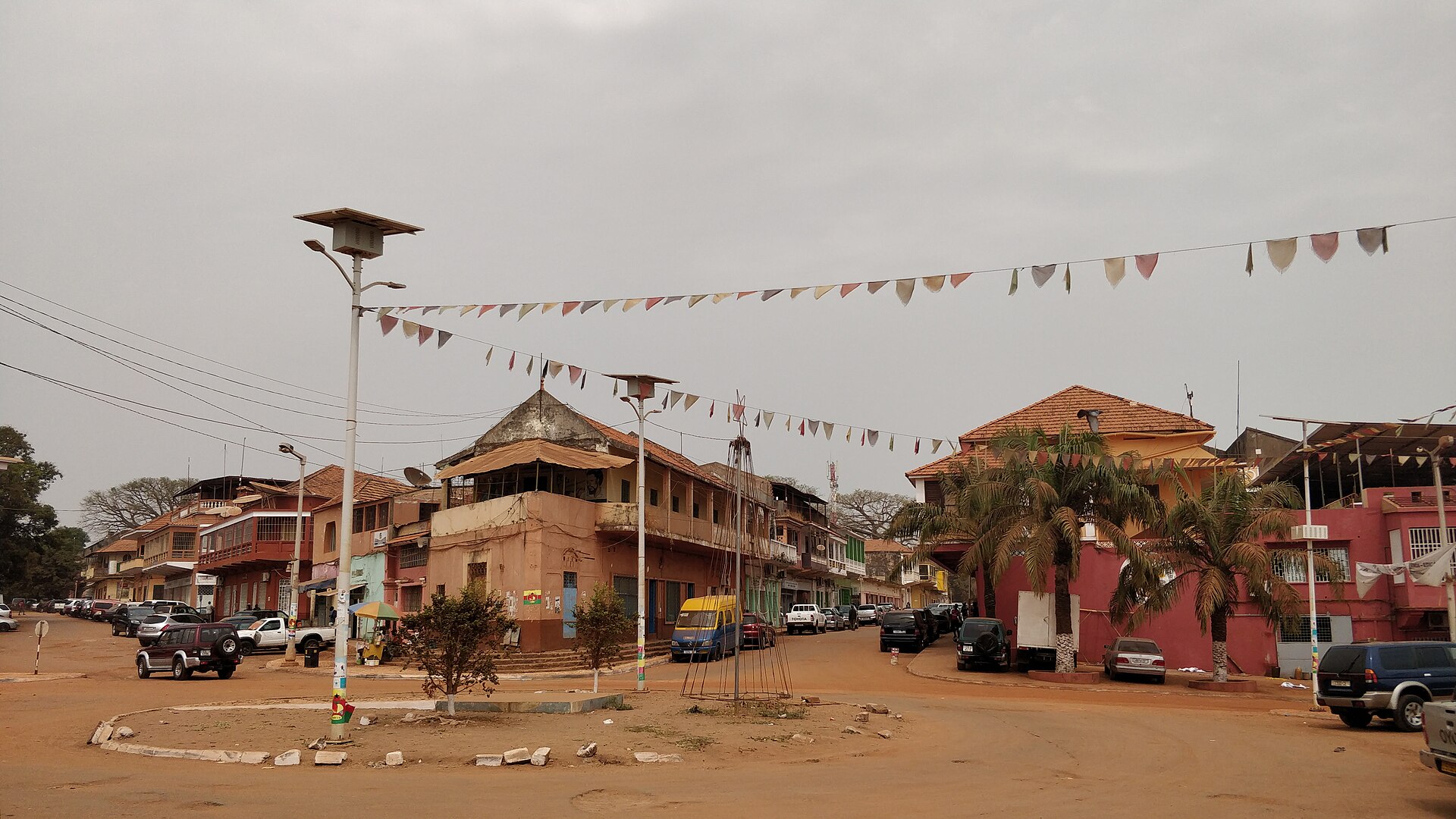 A street corner in Bissau Velho, the old centre of Bissau, with colonial-era buildings, parked cars and strings of coloured bunting across the road