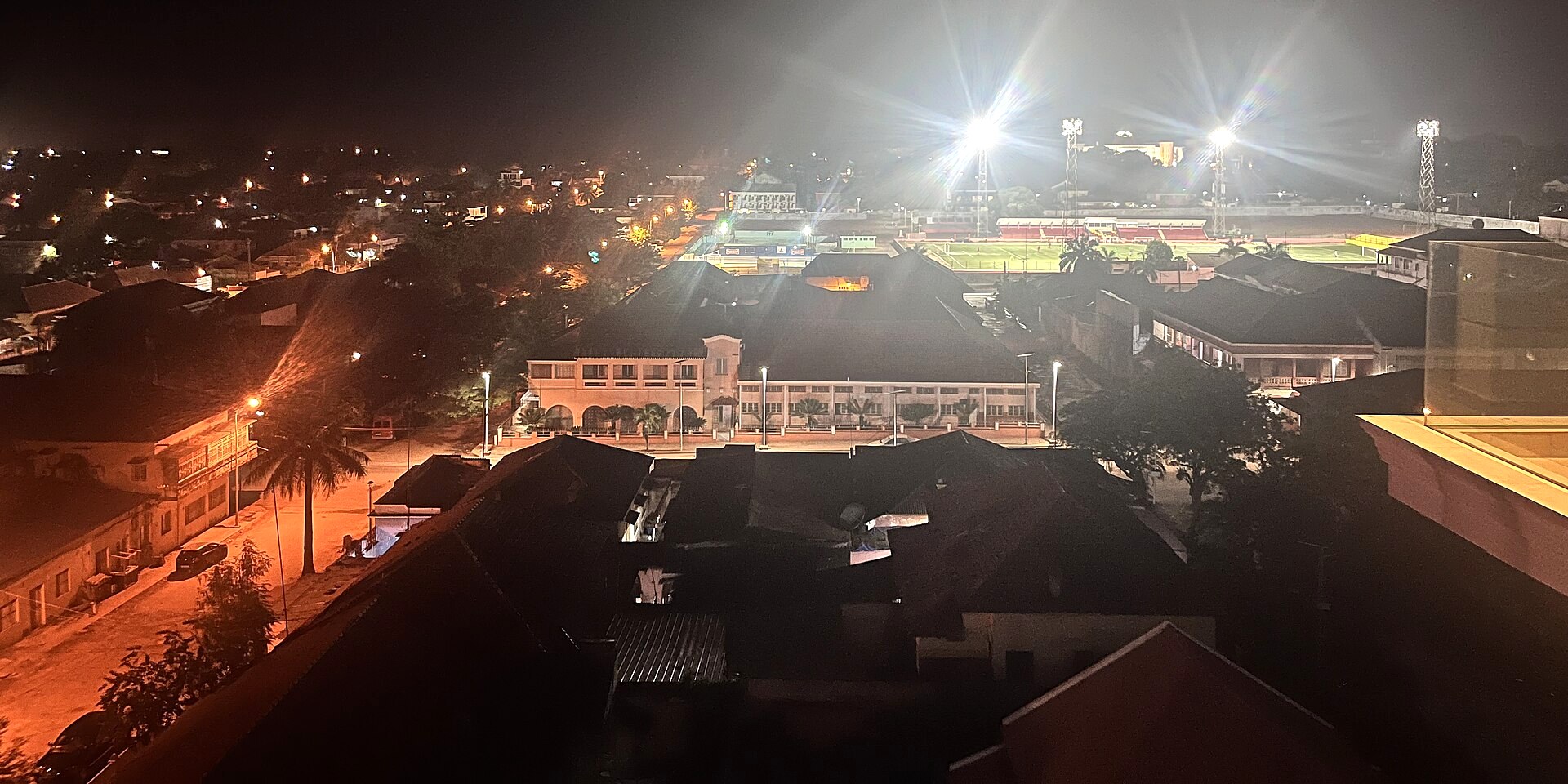 Night view over rooftops in Bissau, Guinea-Bissau, with a floodlit sports ground in the background
