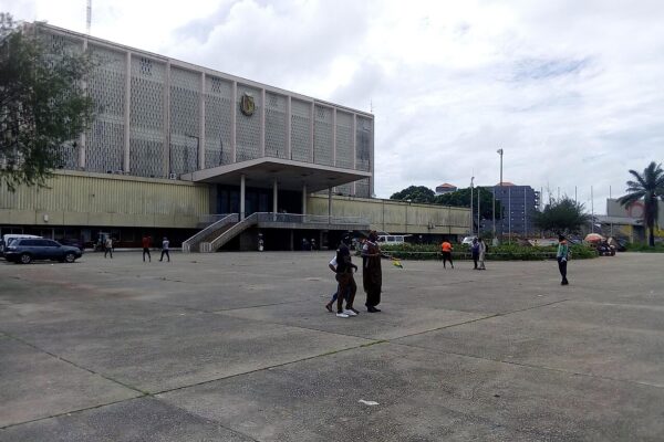 A wide concrete plaza in front of the Palais du Peuple, a large grey government building in Conakry, Guinea
