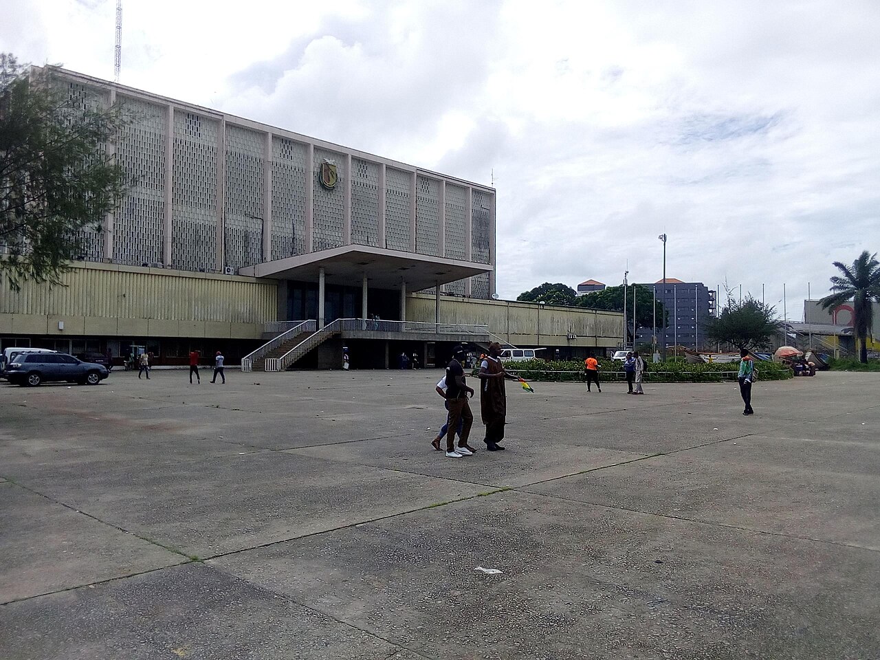 A wide concrete plaza in front of the Palais du Peuple, a large grey government building in Conakry, Guinea