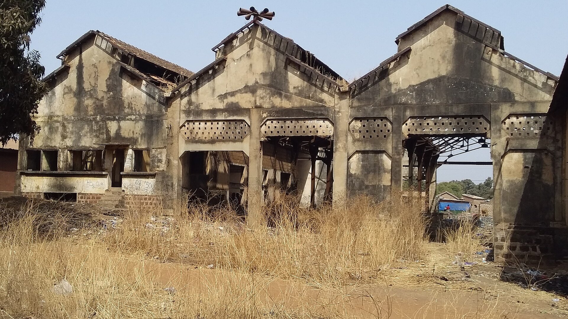 The ruined railway station building at Kankan in eastern Guinea, with a damaged roof and dry grass in front.