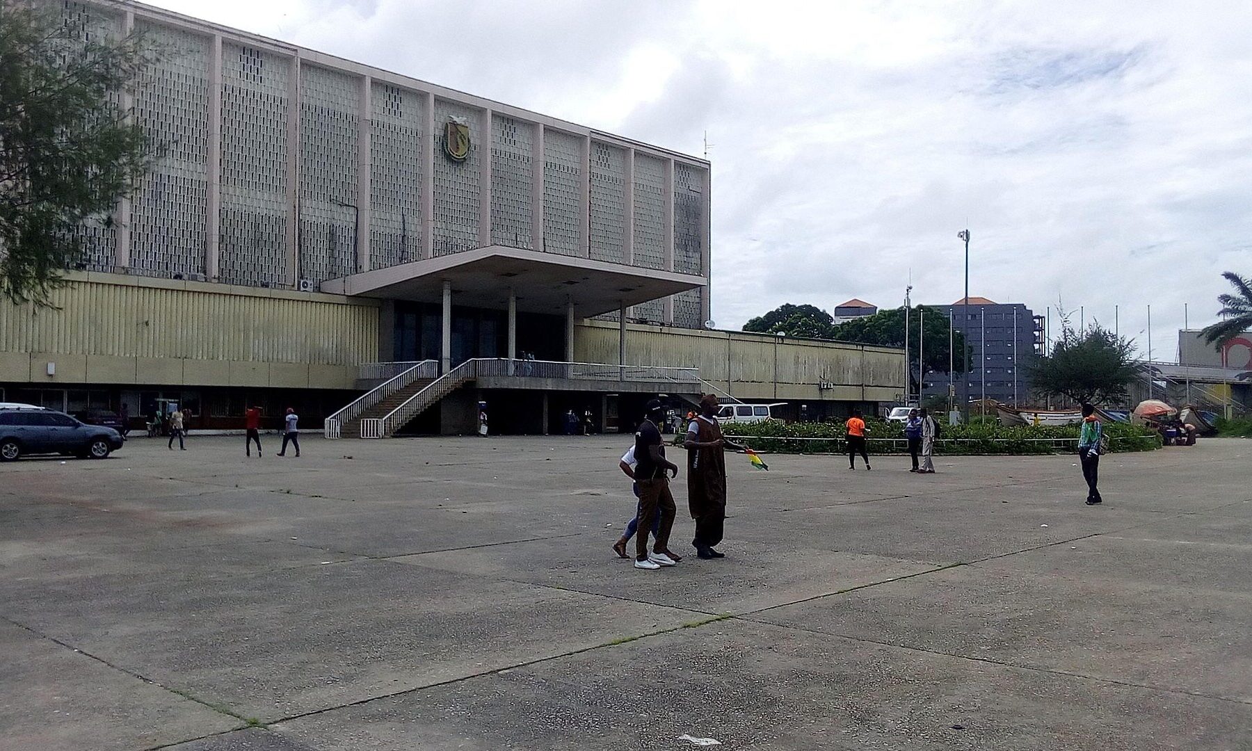 A large mid-century public building with a national emblem on its facade, seen from an open plaza in Conakry, Guinea
