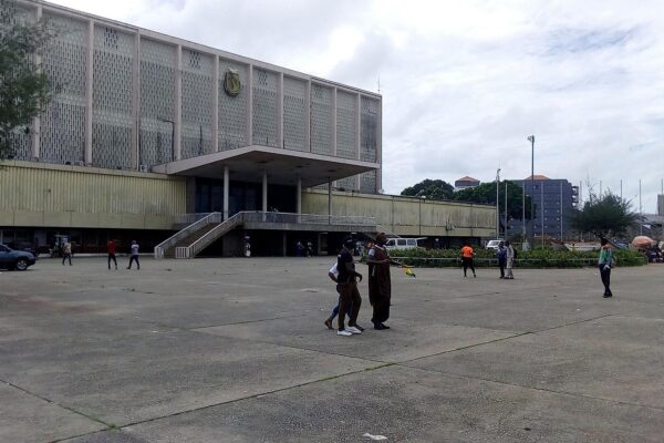 A large mid-century public building with a national emblem on its facade, seen from an open plaza in Conakry, Guinea