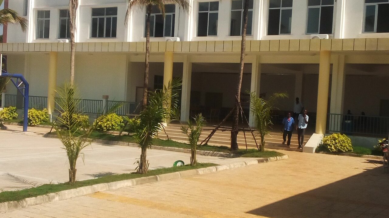 Palm trees, a courtyard and a colonnaded white building where two people walk down steps in Kipe, Conakry