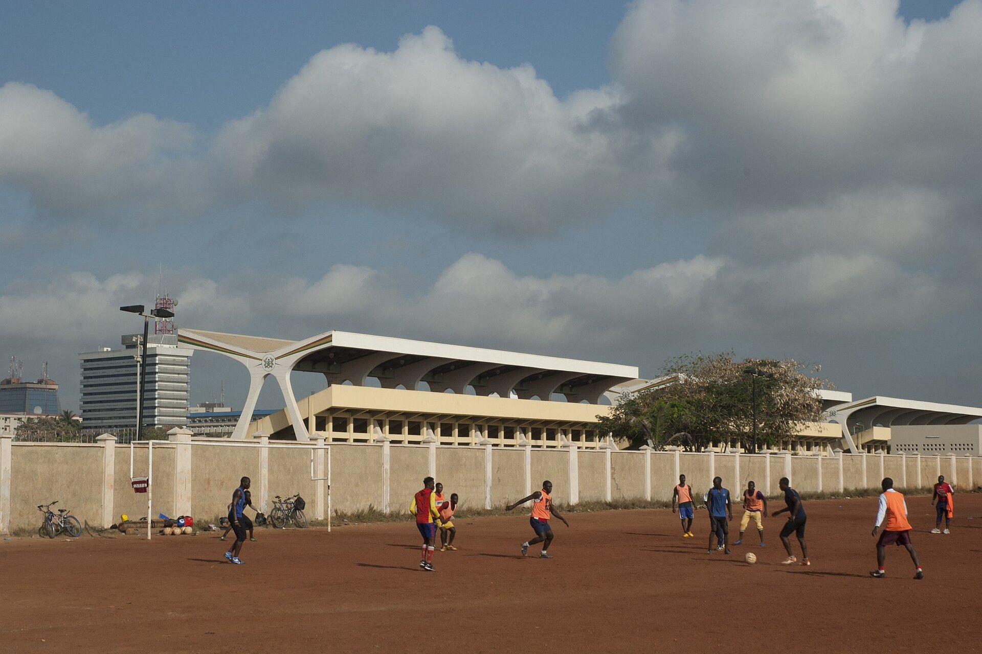 Young men playing football on a dirt pitch in Accra, Ghana, with a large grandstand behind them