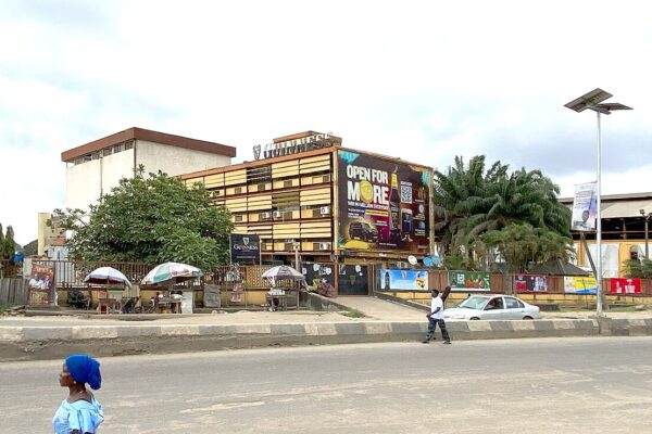 Brick building with a Guinness sign on the roof and a billboard in Lagos, Nigeria, with a pedestrian and parked car in front