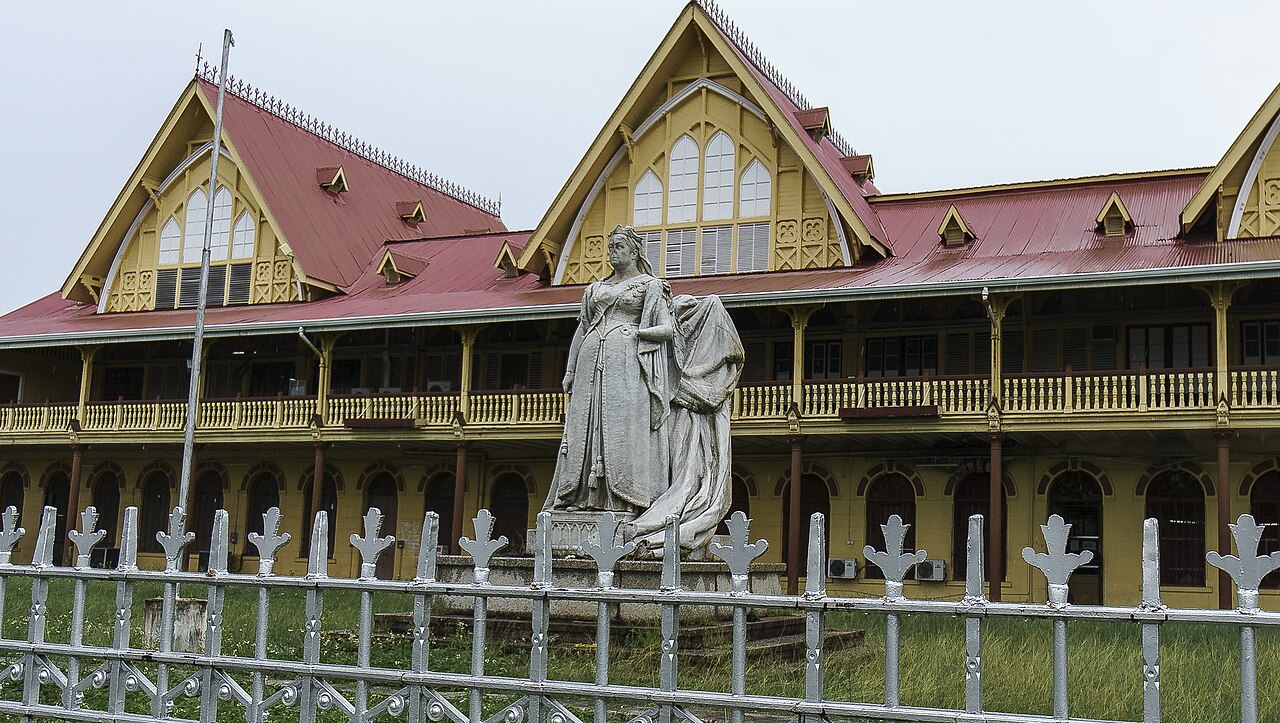 Statue of Queen Victoria in front of the wooden High Court building in Georgetown, Guyana, behind an iron fence