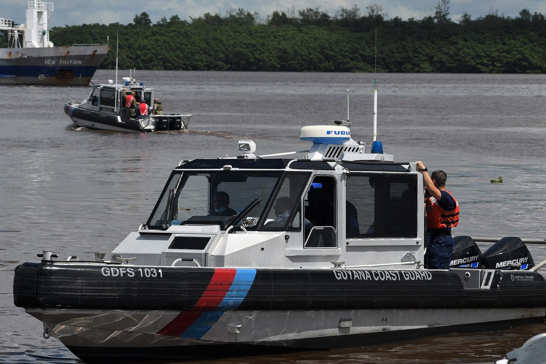 A Guyana Coast Guard patrol boat on the Demerara River with a cargo ship in the background