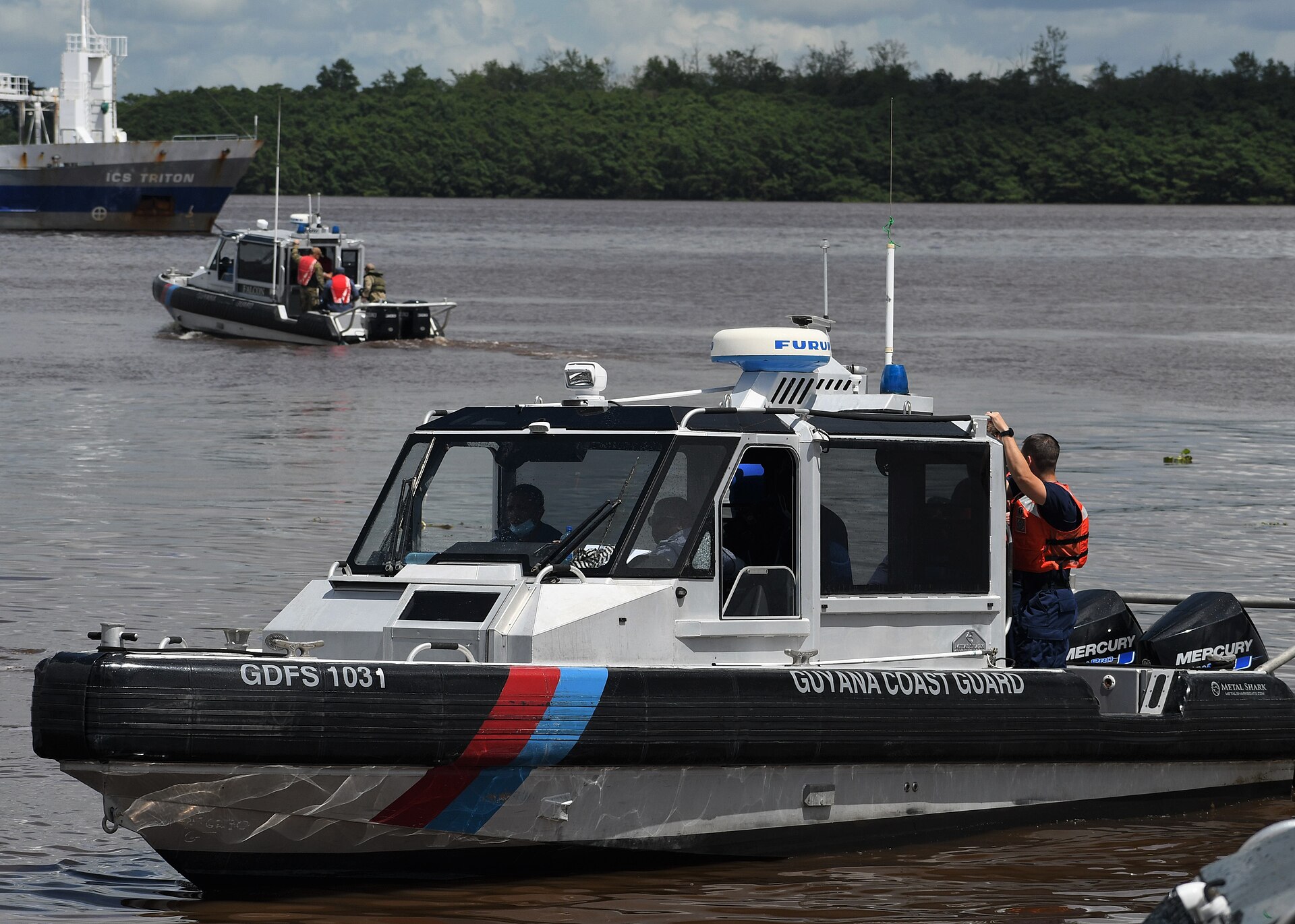 A Guyana Coast Guard patrol boat on the Demerara River with a cargo ship in the background