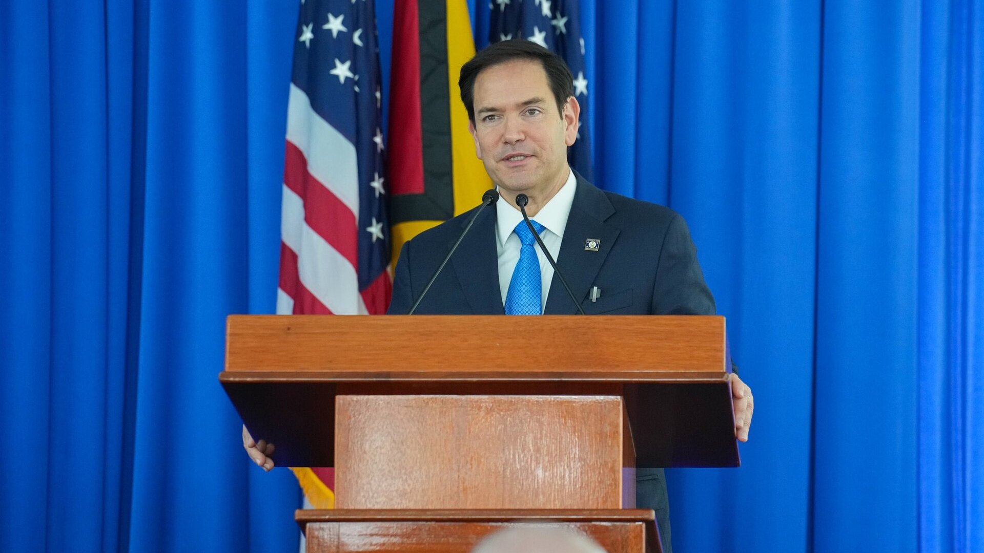 US Secretary of State Marco Rubio speaking at a lectern in front of US and Guyanese flags in Georgetown