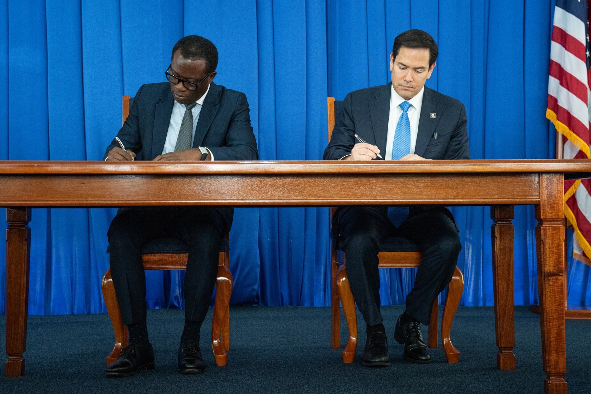 US Secretary of State Marco Rubio and Guyana's Foreign Minister Hugh Todd signing a document at a table with a US flag