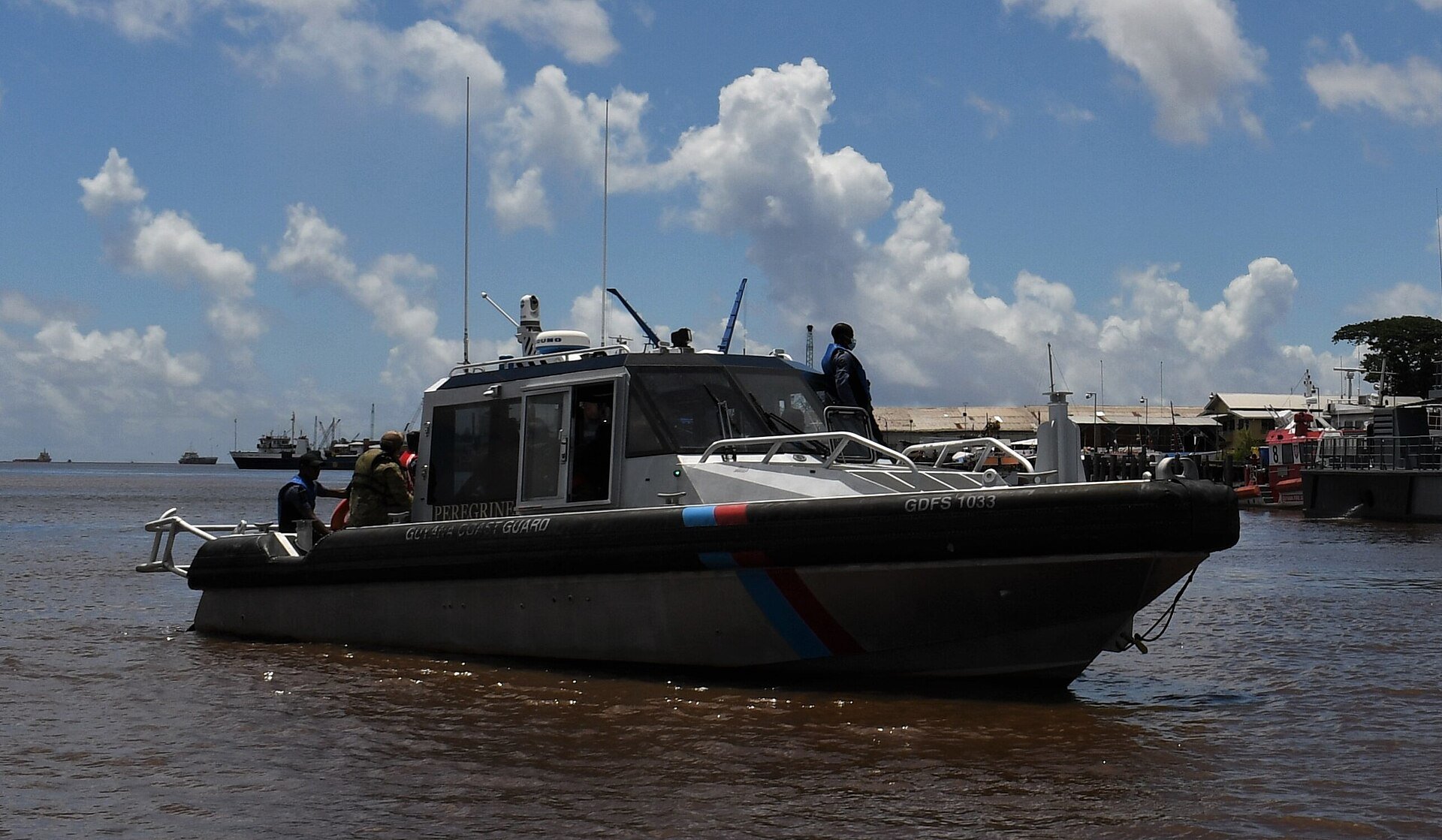 Guyana Coast Guard patrol boat Peregrine on the brown Demerara River near Georgetown with a ship in the distance