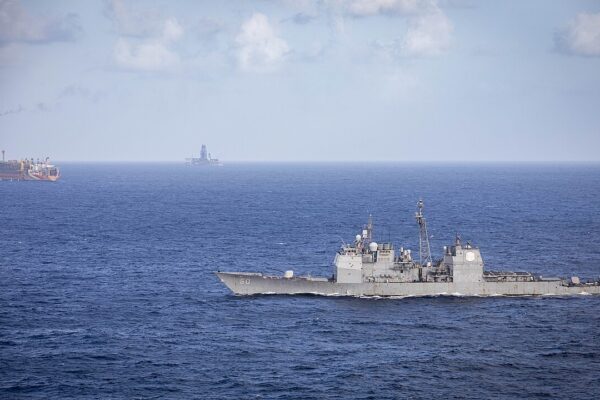 A US Navy cruiser sails past a floating oil production vessel in the Stabroek Block off Guyana