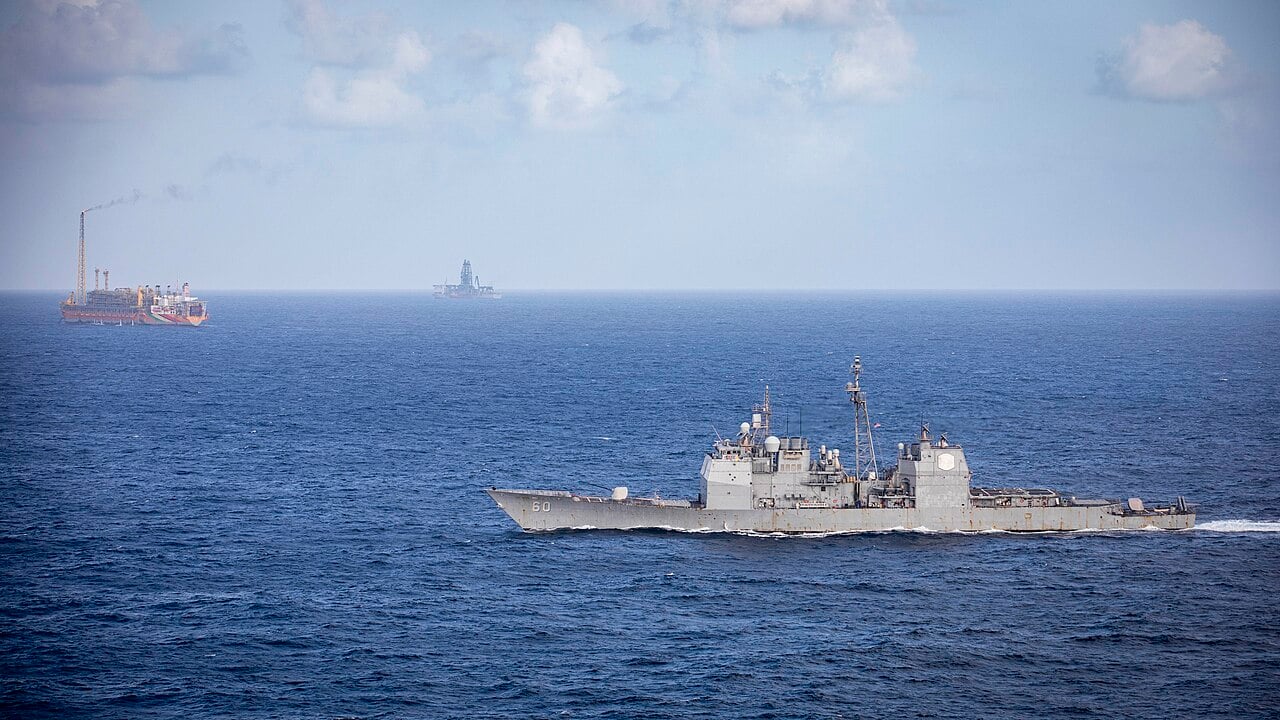 A US Navy cruiser sails past a floating oil production vessel in the Stabroek Block off Guyana