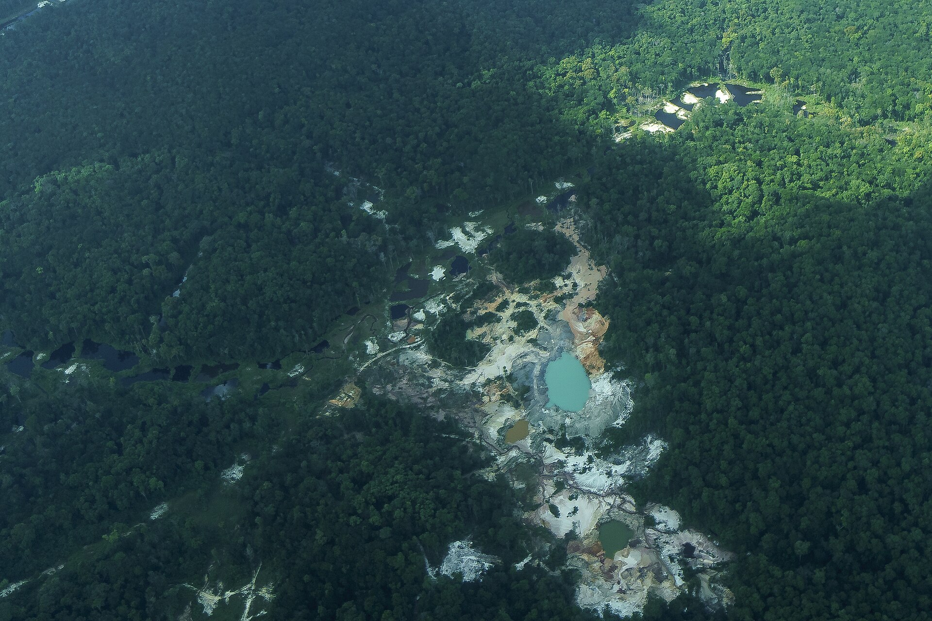 Aerial view of a gold-mining scar and a turquoise pit lake cut into dense rainforest in Guyana