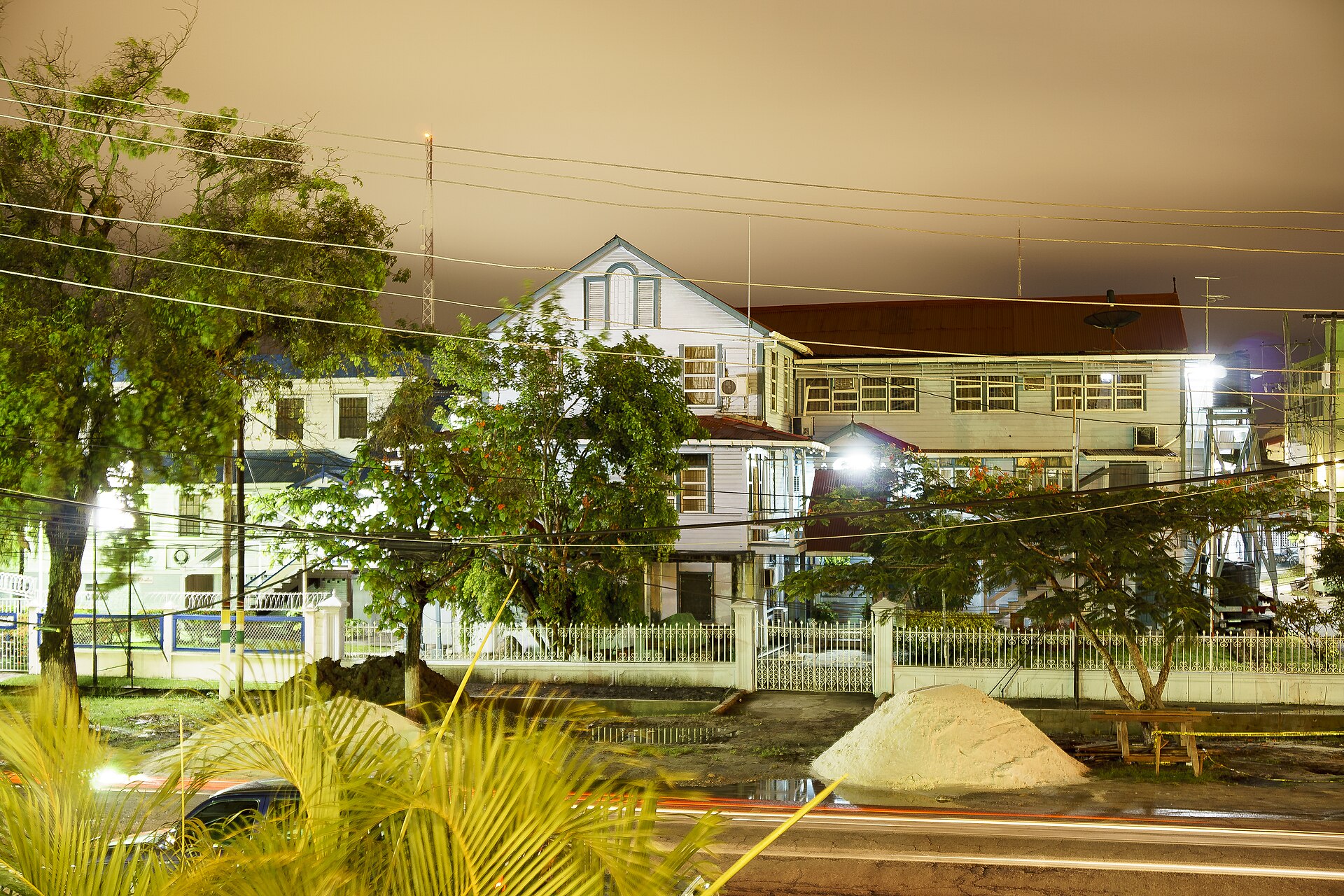 Timber houses behind a white fence and trees on a street in Georgetown, Guyana, photographed at night