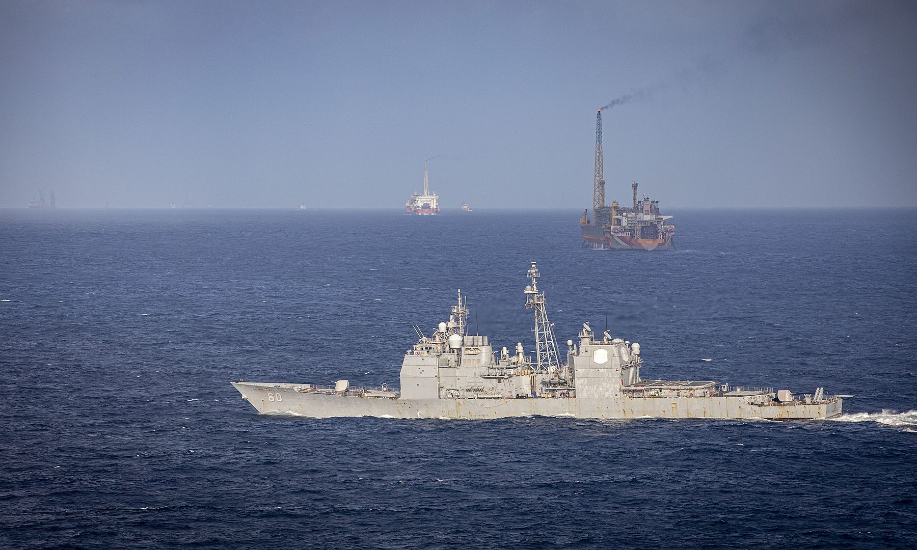 A US Navy cruiser passes a floating production vessel with a flare in the Stabroek Block off Guyana