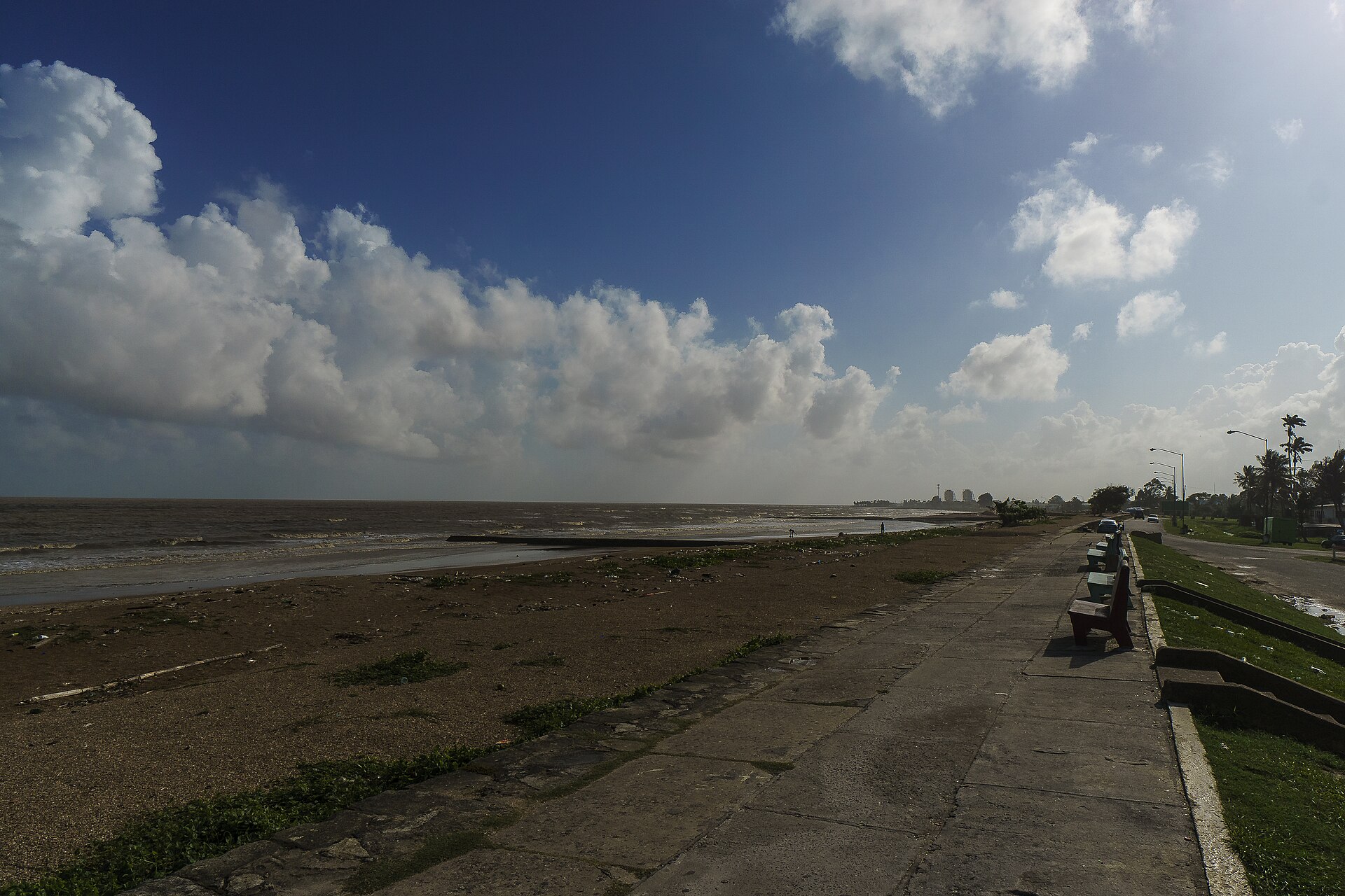 The seawall promenade and the Atlantic shore in Georgetown, Guyana, under a blue sky with clouds