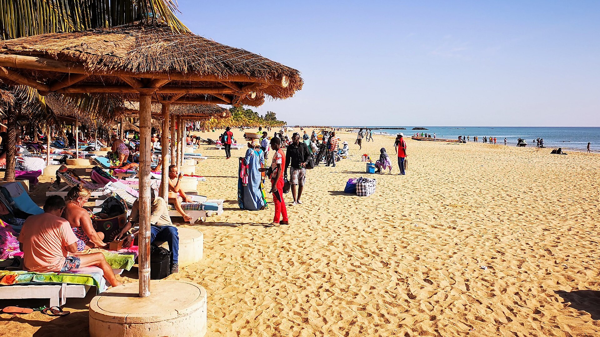 Sunbathers under thatched parasols and people walking on the wide sandy beach at Saly, Senegal