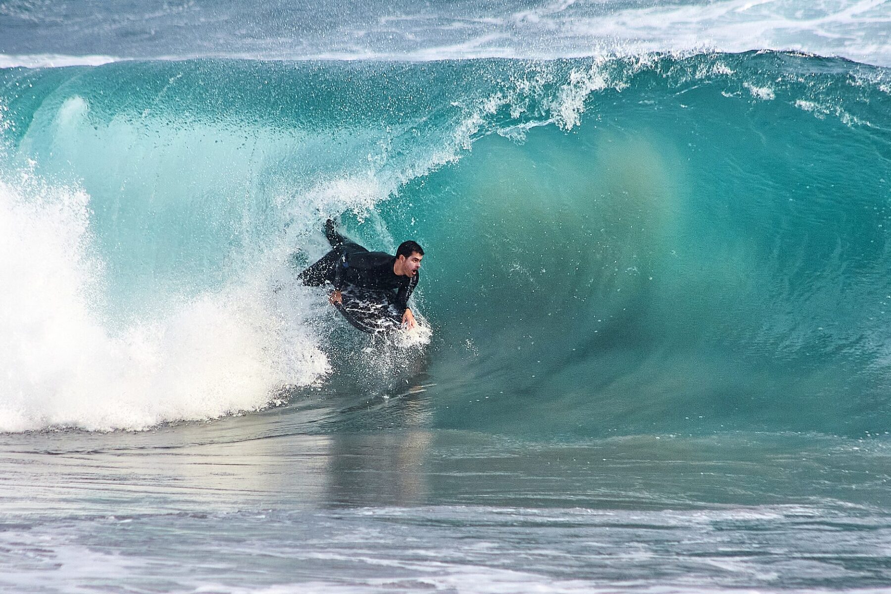 A bodyboarder rides inside a curling turquoise wave at Playa Explosivos in Punta Negra, Peru